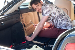 Unprofessional man repairing his own car interior with amateur tools on a sunny day.