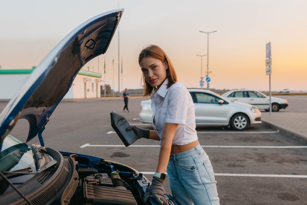 woman with an open hood in a car pours technical fluid, oil, brake fluid on the road.