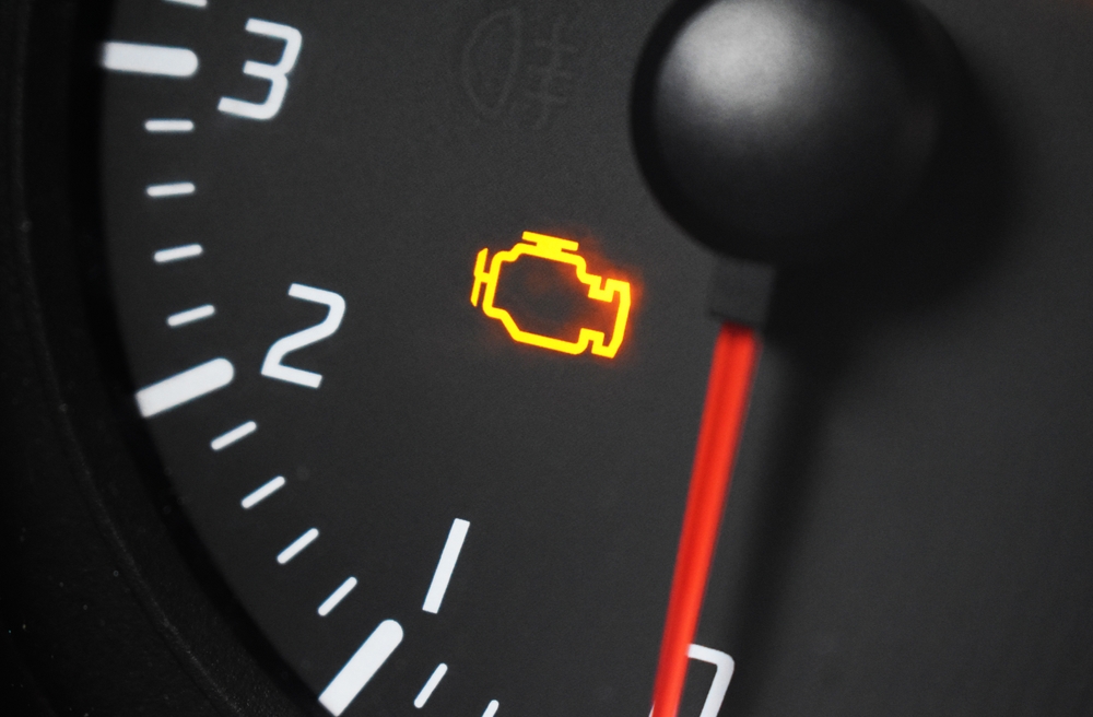Close up shot of illuminated orange engine management warning light on the dashboard of a modern car.